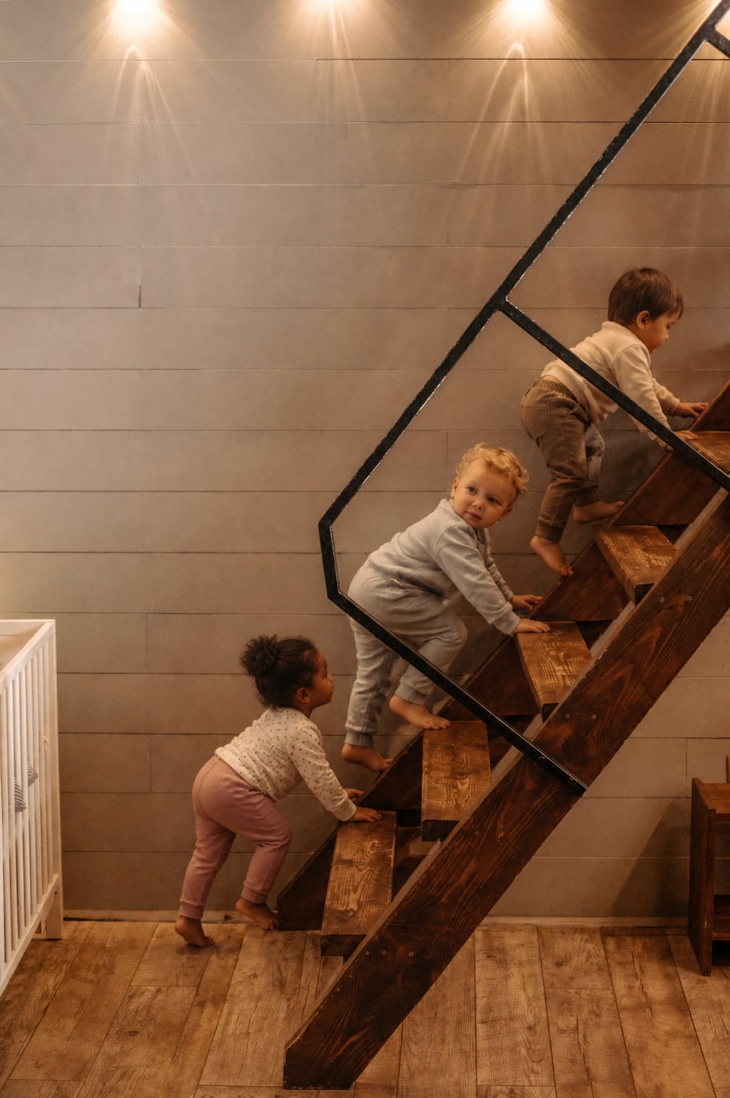 Three toddlers climbing wooden stairs together on hands and feet.